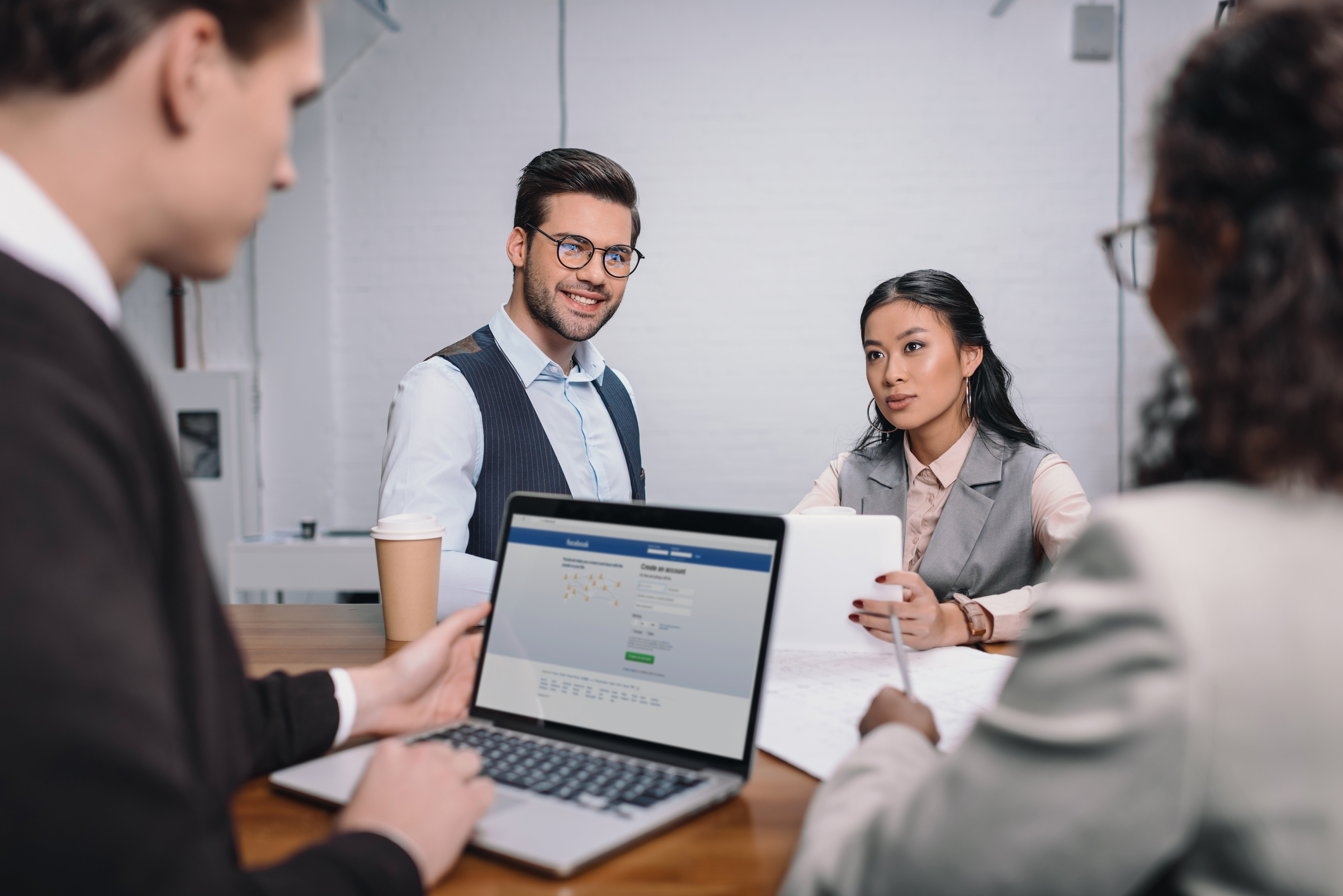 Compañeros de trabajo dialogando mientras uno de ellos tiene su pagina de Facebook en su computador.
